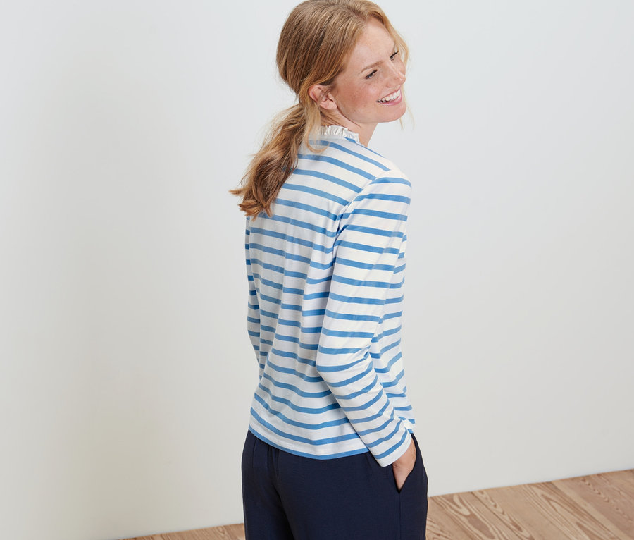 Žena pózuje v tričku s dlouhým rukávem a volánky.