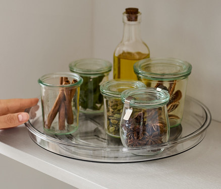 Ruka sáha na otočný talíř s kořením na polici.