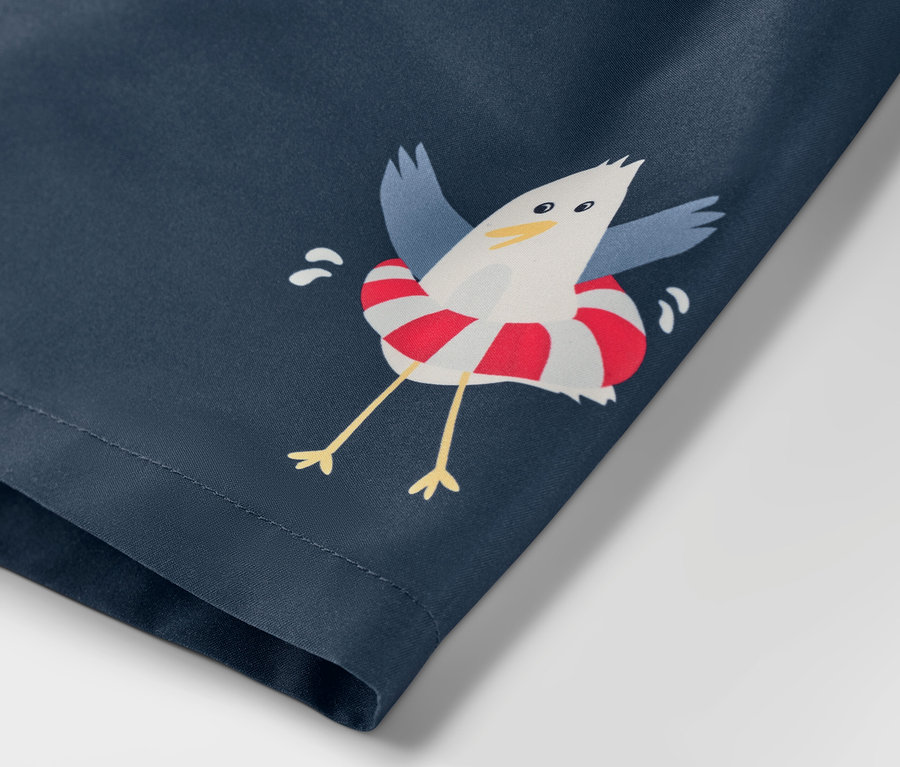 Detail chlapeckých koupacích šortek s motivem moře a potiskem racka v záchranném kruhu.