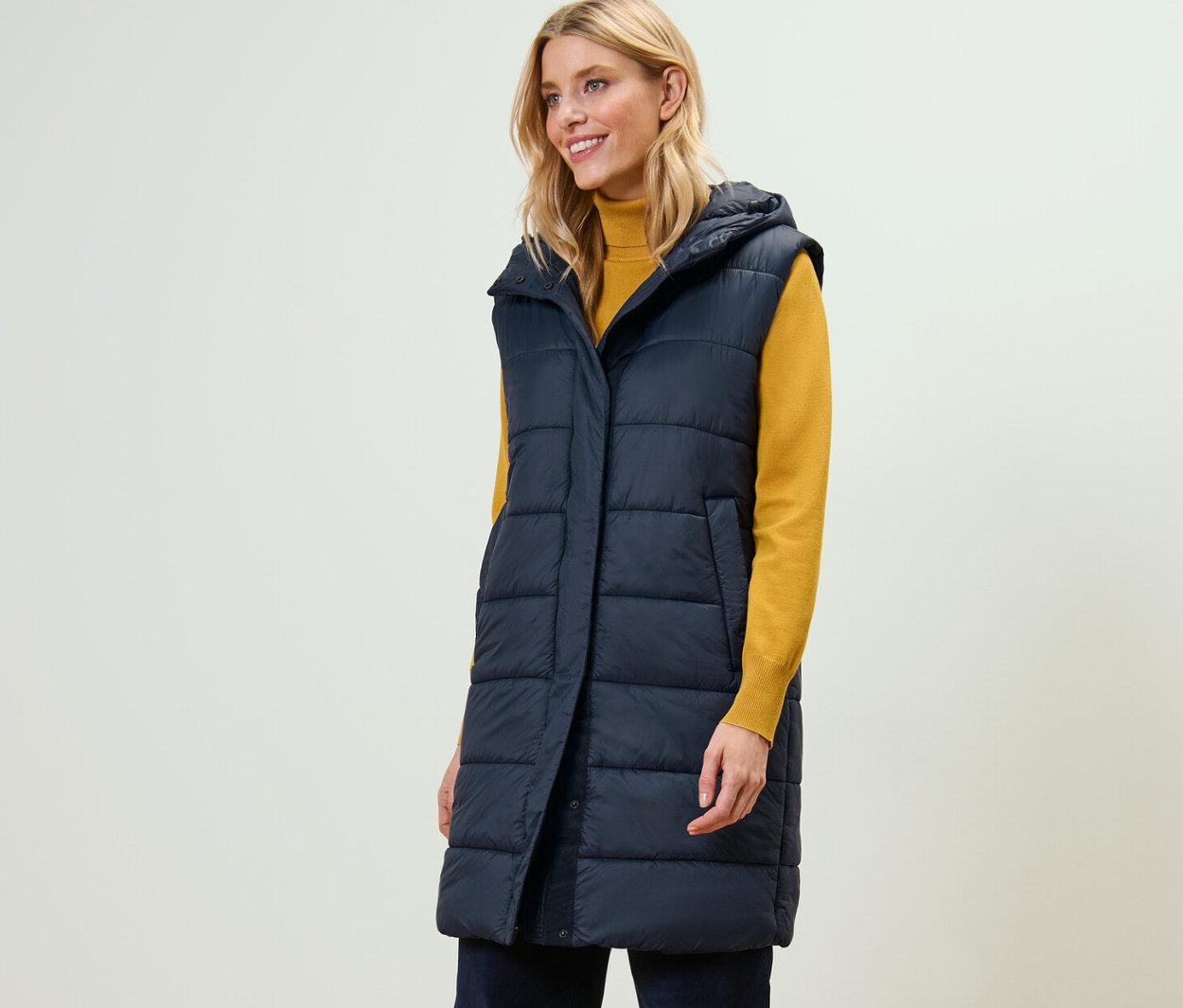 Žena má na sobě dlouhou prošívanou vestu s kapucí.