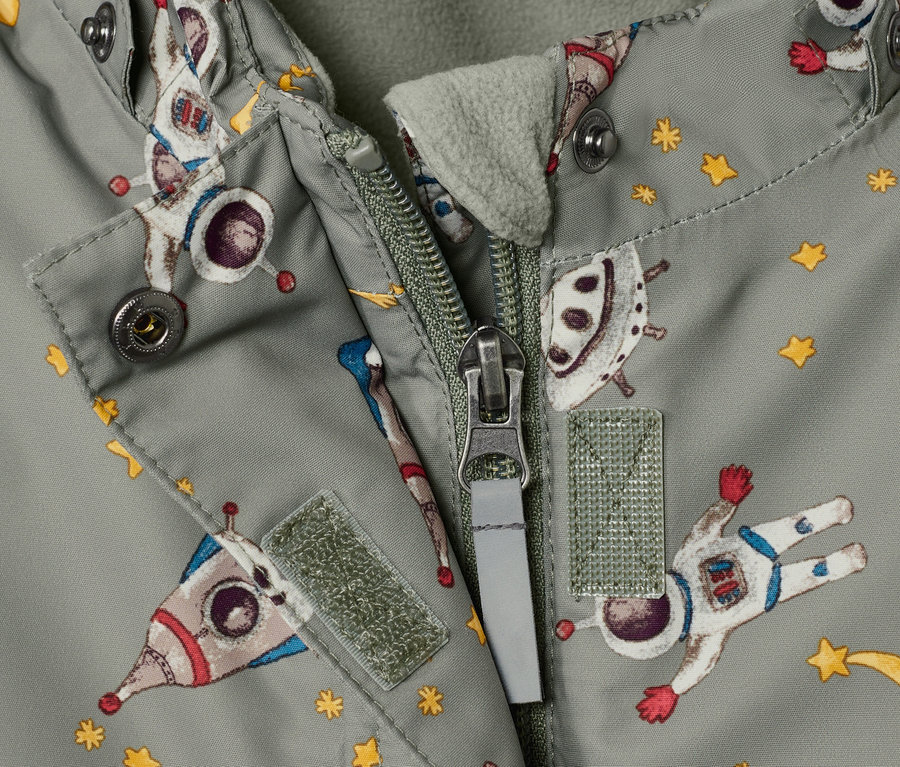 Detail dětské zimní kombinézy s potiskem vesmíru a rozepnutým zipem.