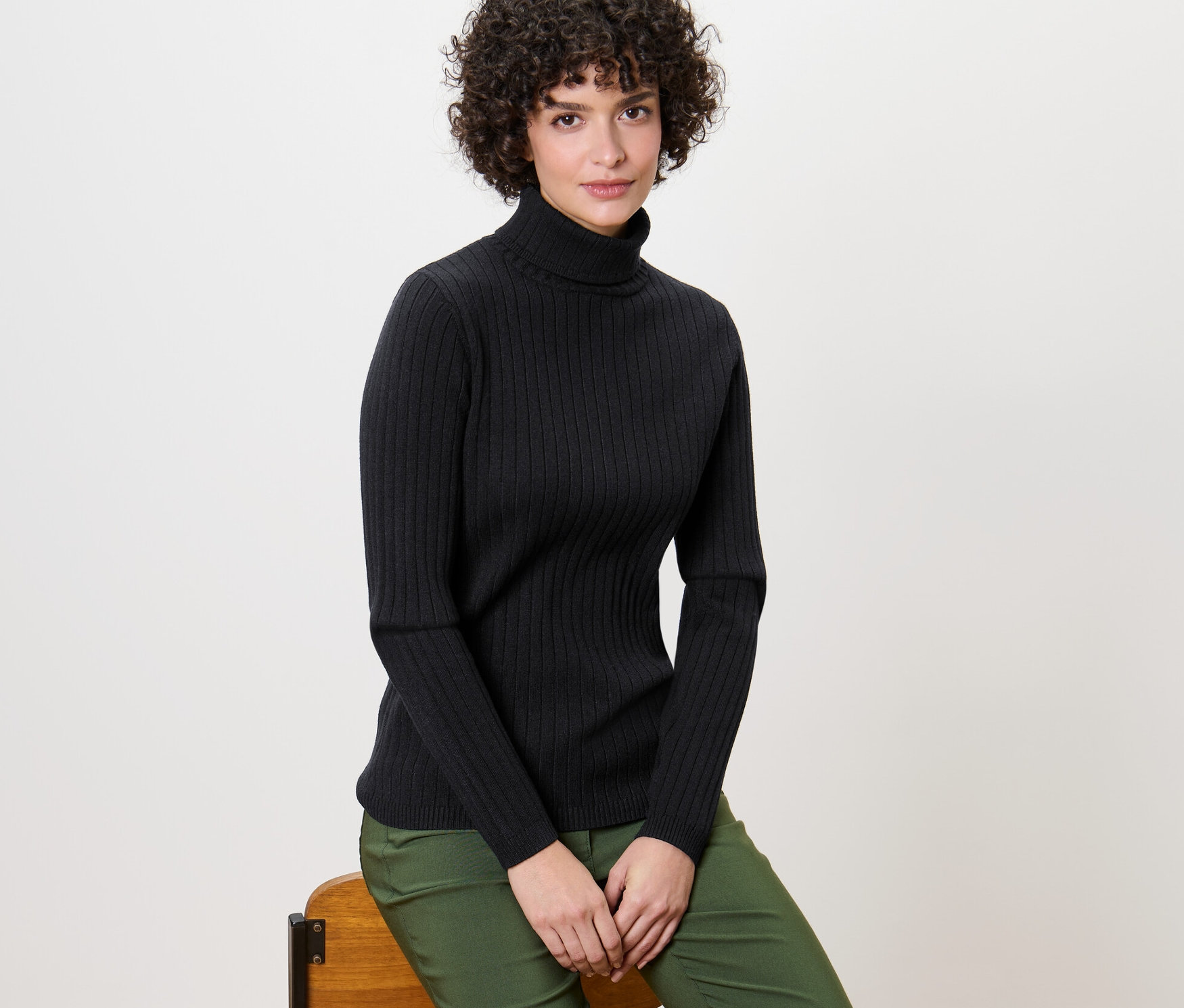 Žena sedí na židli a má na sobě černý žebrovaný rolák.