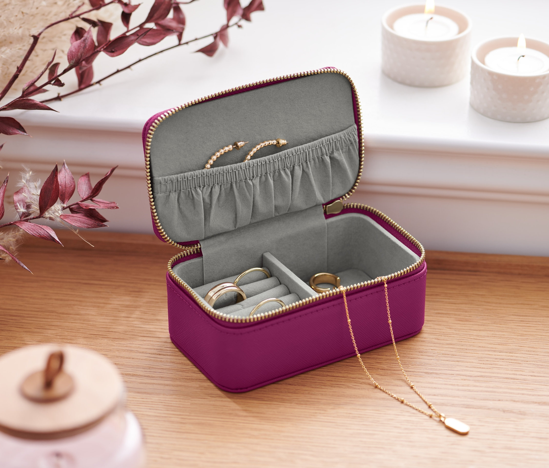 Otevřená malá šperkovnice fialové barvy se zlatým zipem na dřevěném stole. Uvnitř jsou prsteny, náhrdelník a náramek.