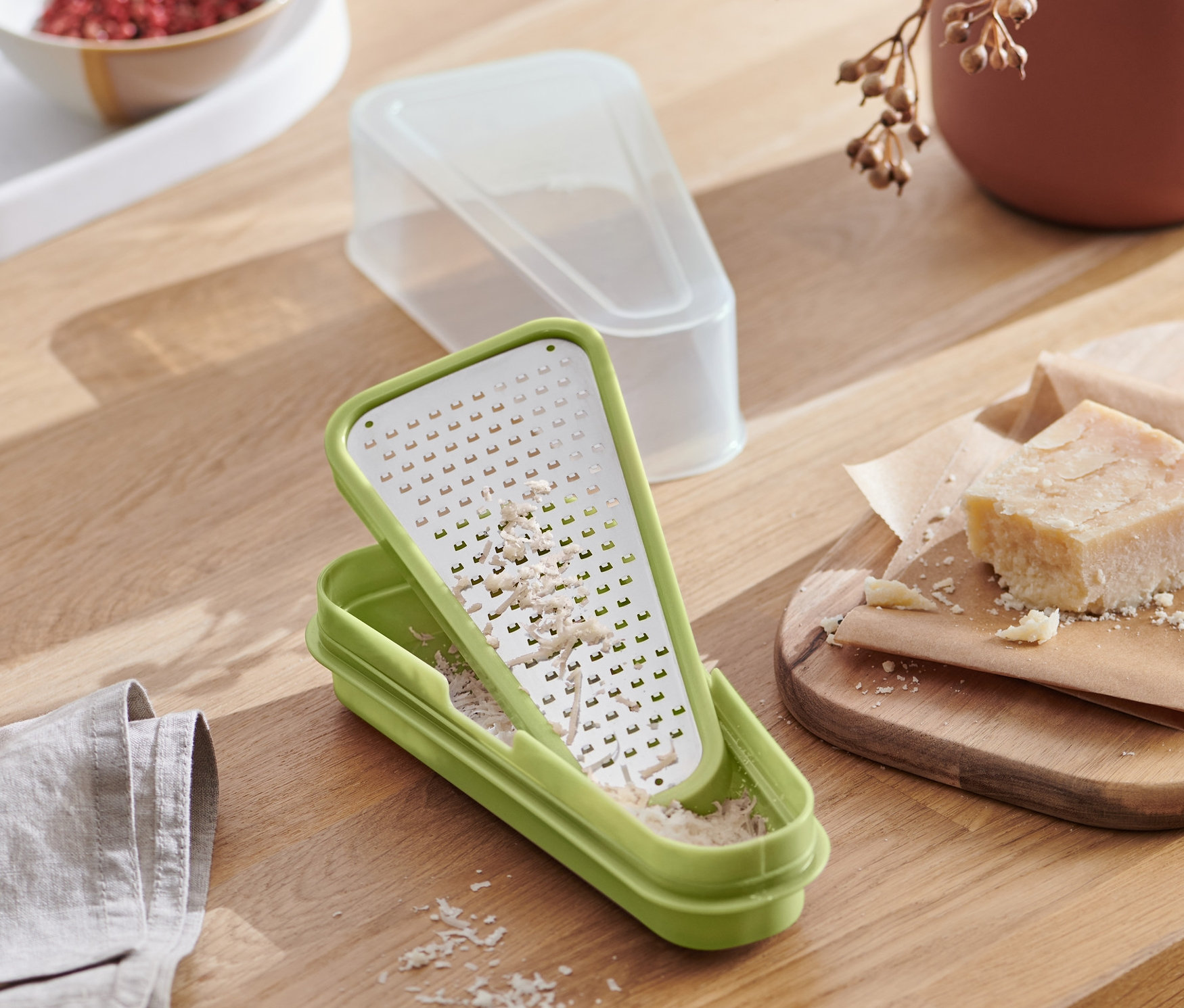 Zelené struhadlo na parmazán 2 v 1 s nastrouhaným sýrem na dřevěném stole s jídlem.