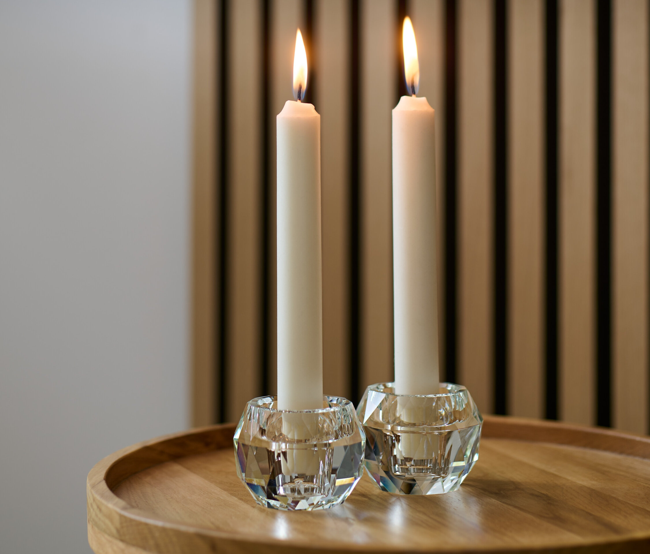 Dva skleněné svícny s hořícími svíčkami na dřevěném stole.