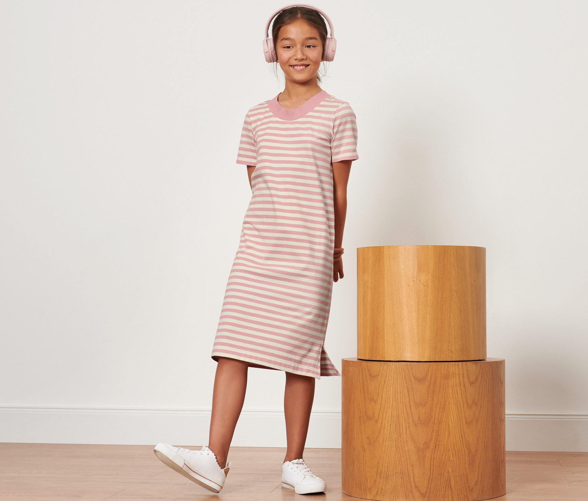 Dívka s růžovými sluchátky stojí v pruhovaných šatech.