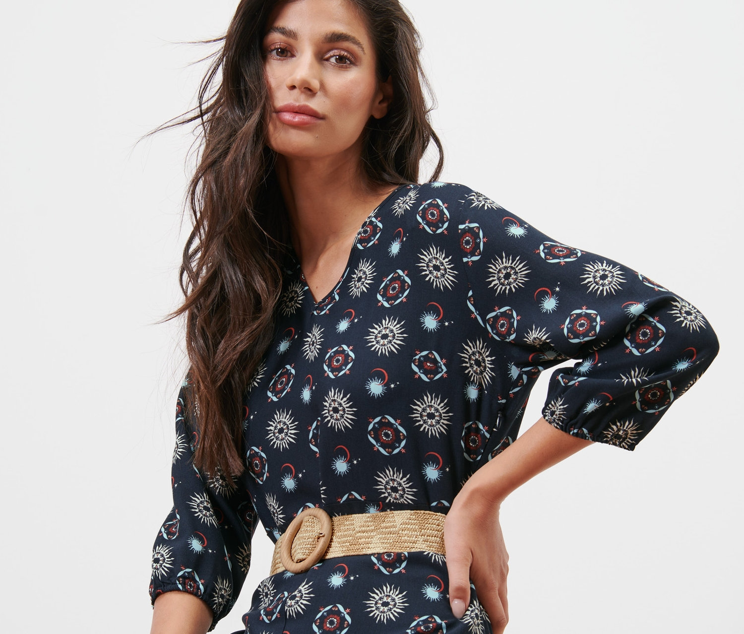 Žena pózuje v tmavě modrých šatech s motivem slunce a měsíce a s páskem.