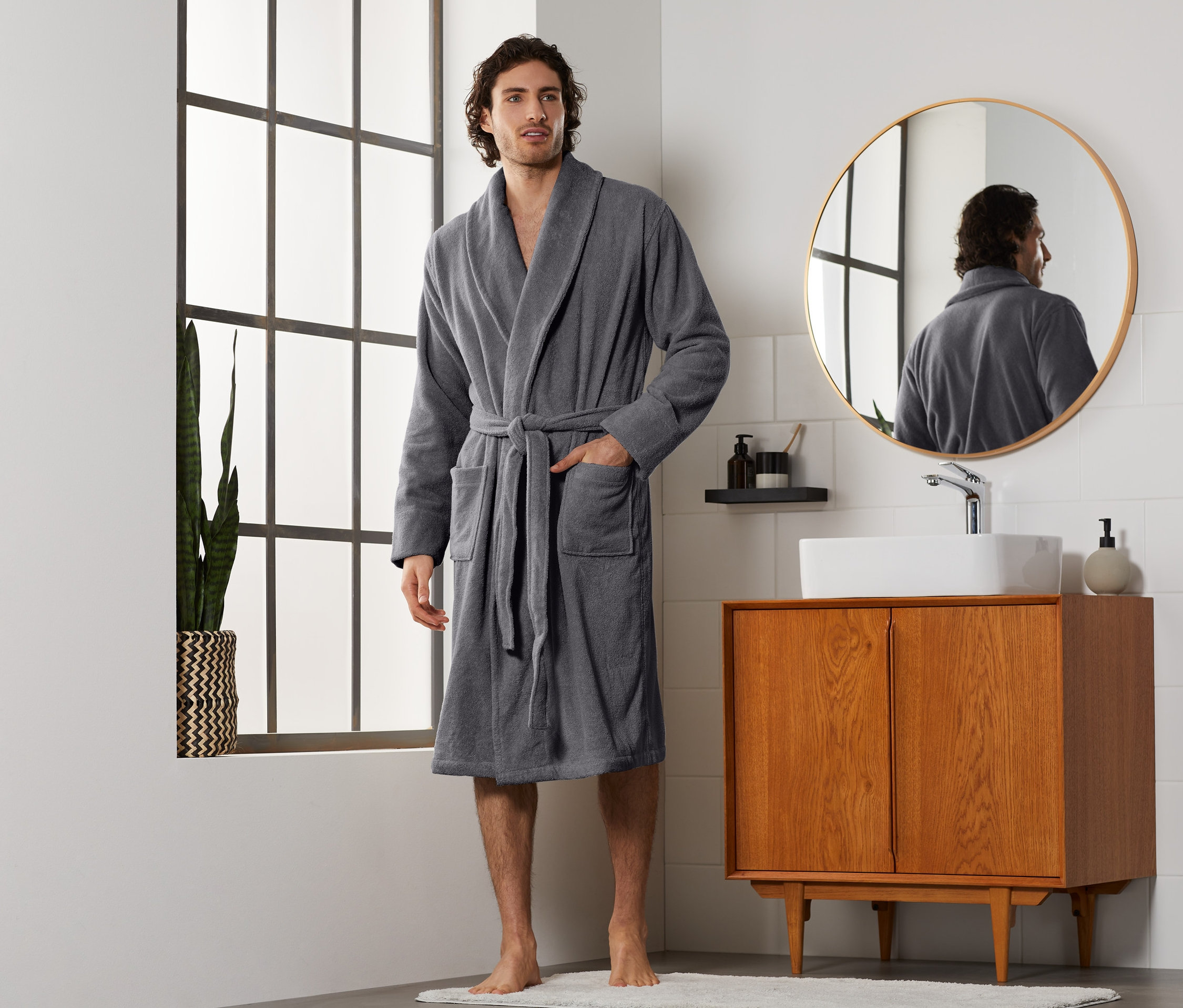 Muž v šedém županu stojí v koupelně.