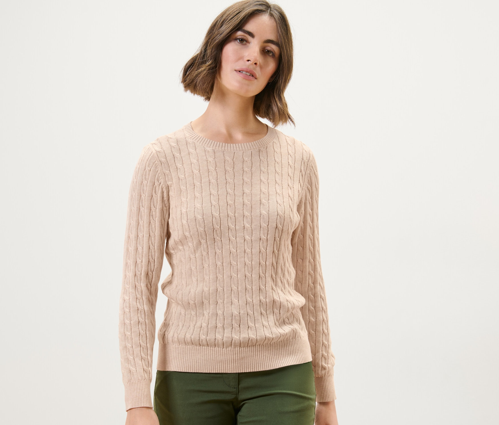 Žena má na sobě krémový svetr s copánkovým vzorem.