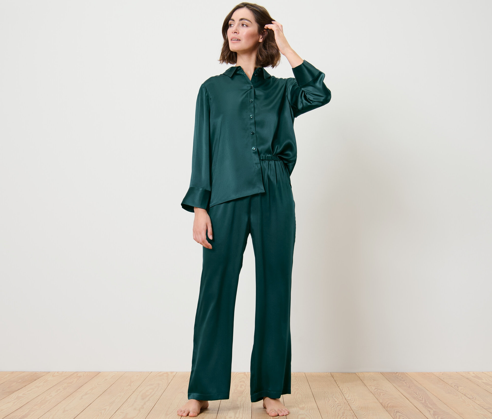 Žena má na sobě hedvábné pyžamo a pózuje v místnosti.