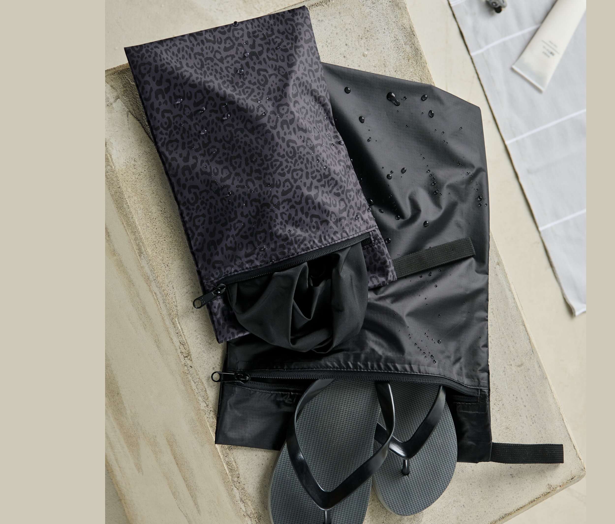 Dva voděodolné sáčky na betonovém povrchu. V jednom jsou černé žabky, v druhém černé oblečení.