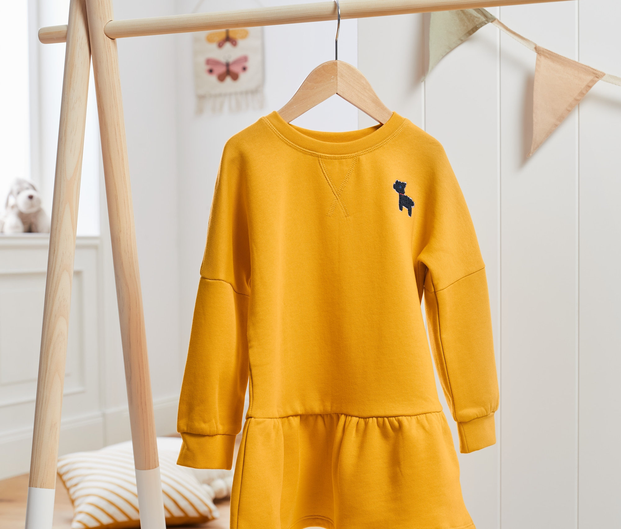 Žluté teplákové šaty visí na dřevěném stojanu.