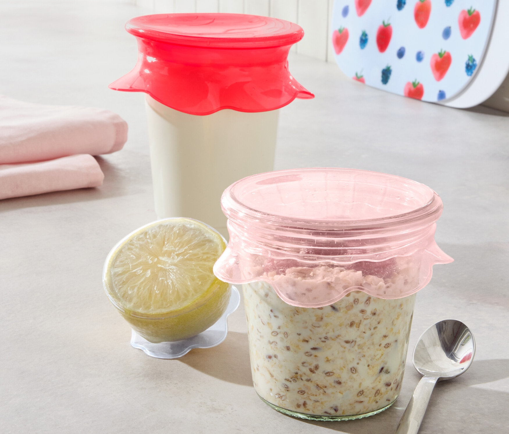 Dvě sklenice s obsahem jsou zakryté silikonovými víčky pro uchování čerstvosti, 3 ks. Vedle je citron a lžíce.