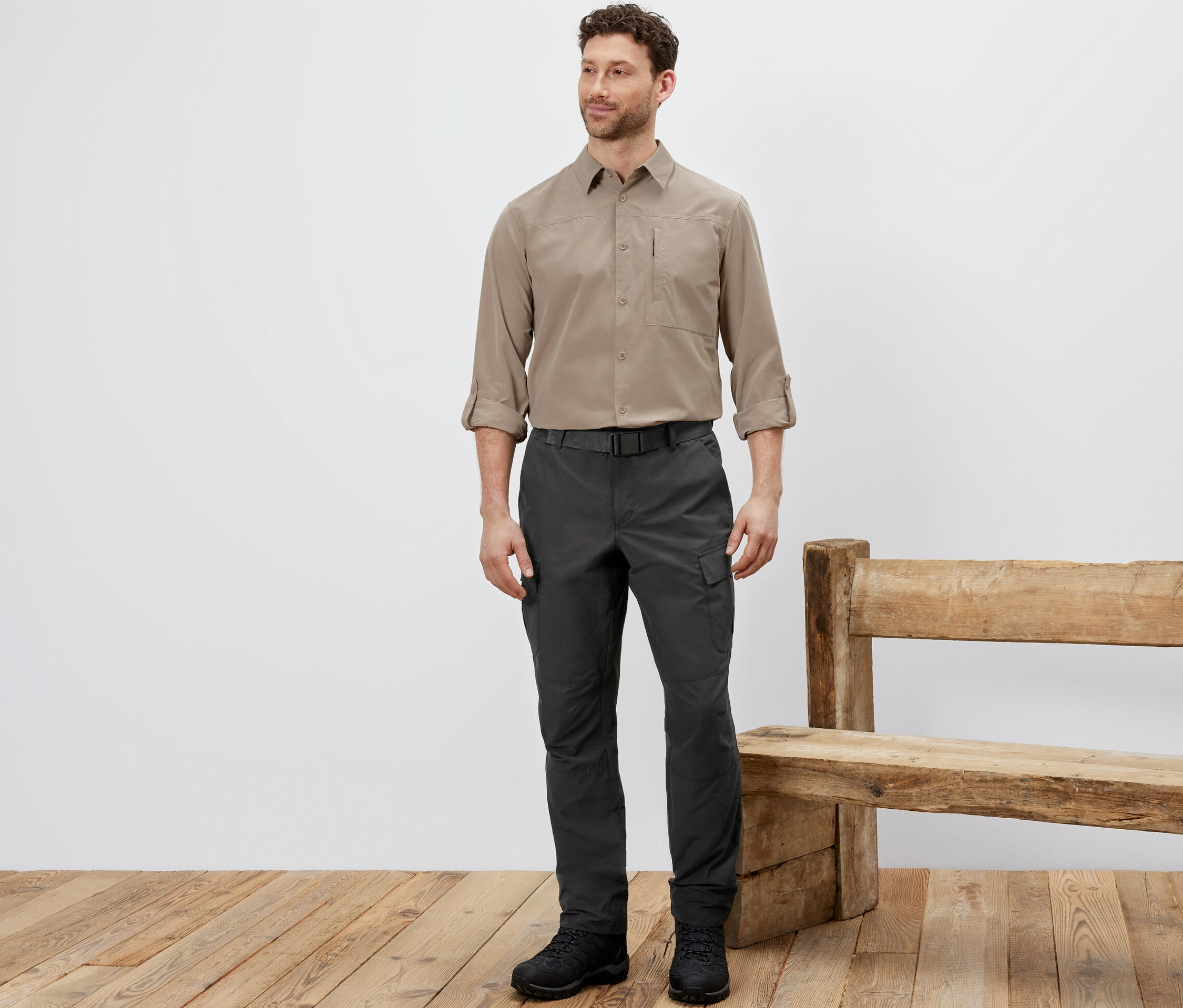 Muž stojí a má na sobě outdoorové kalhoty s ochranou proti komárům, béžovou košili a černé boty.