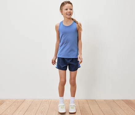 Usmívající se dívka stojí a má na sobě modrý sportovní top a sportovní šortky.