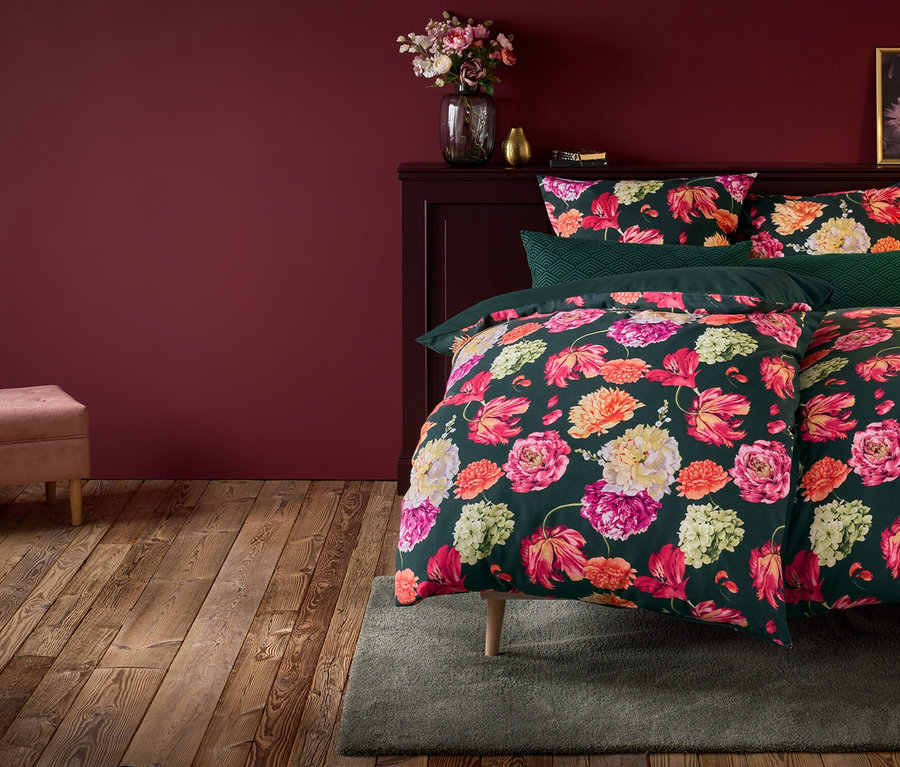 Květinové povlečení na posteli s nočním stolkem, lampou a růžovou lavicí.