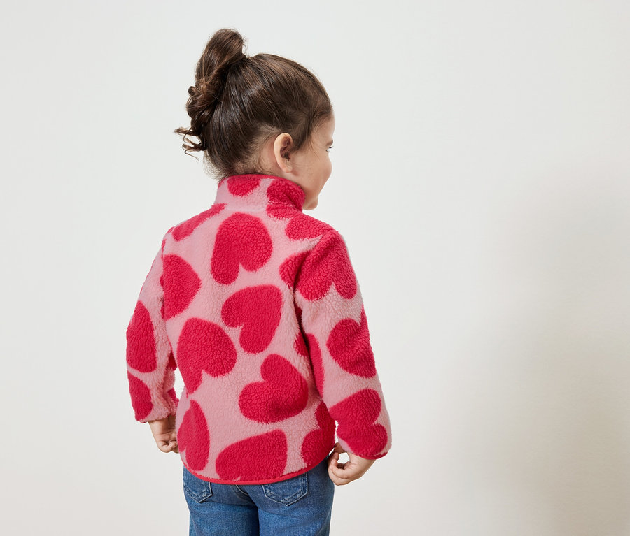 Malá holčička v mikině s červenými srdíčky, dívá se doprava.