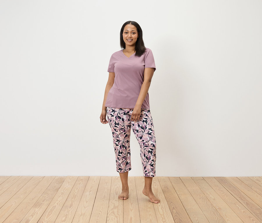 Žena stojí a má na sobě fialové tričko a květinové kalhoty.