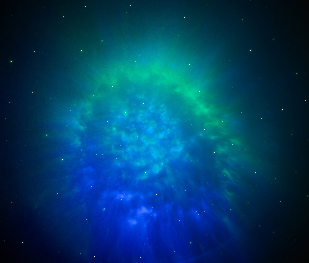 Rozmazaná fotografie hvězdokupy v odstínech modré a zelené barvy.