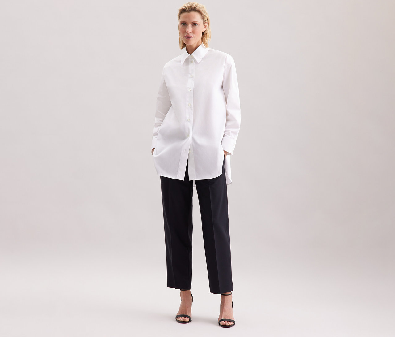 Žena v bílé dlouhé halence oversize Seidensticker a černých kalhotách.