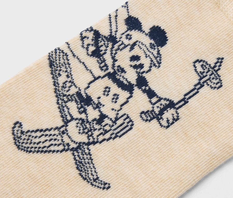 Detail béžové ponožky s tmavě modrým vzorem Mickeyho Mouse na lyžích.