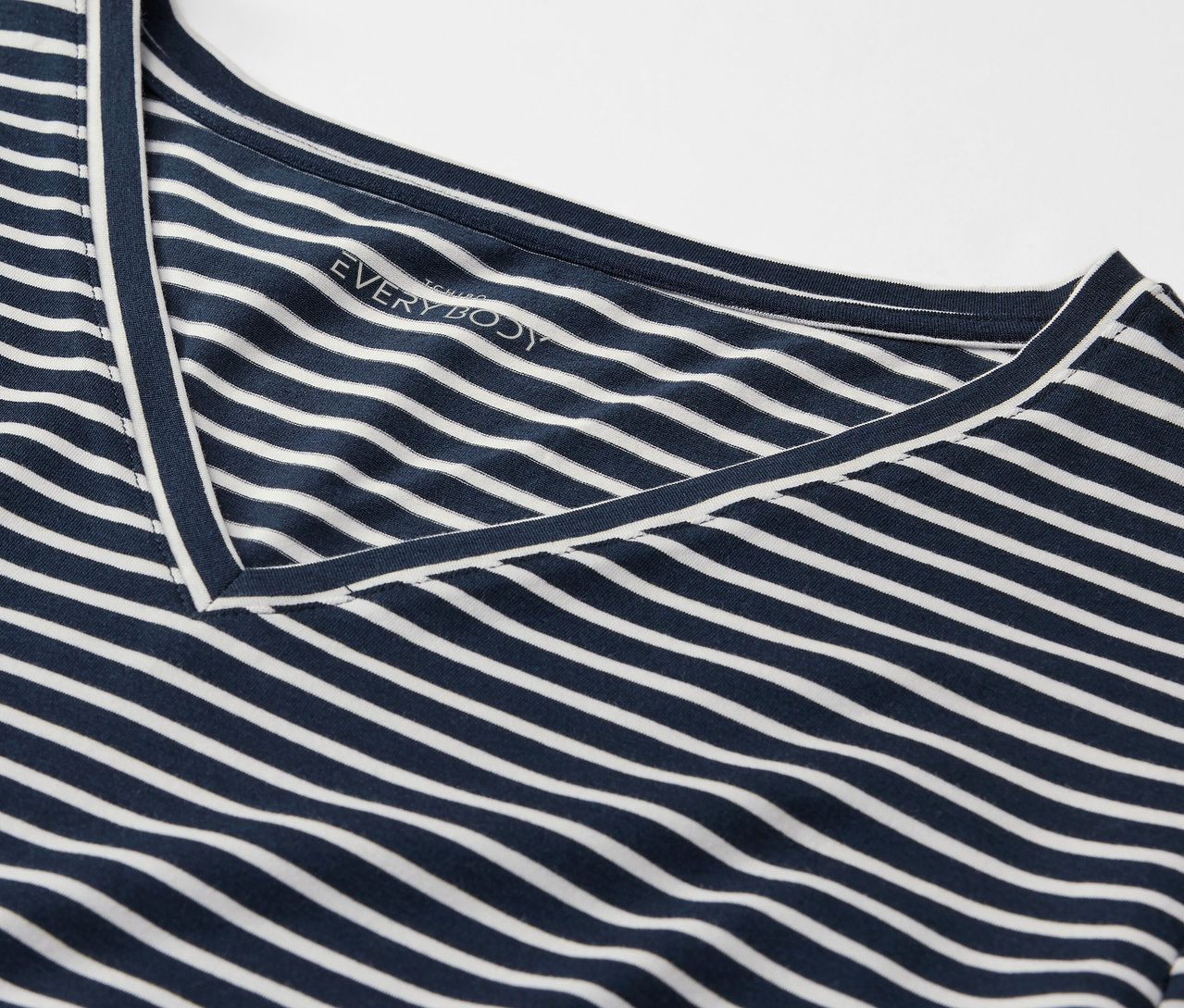 Detail modrého trička s bílými pruhy a výstřihem do V.