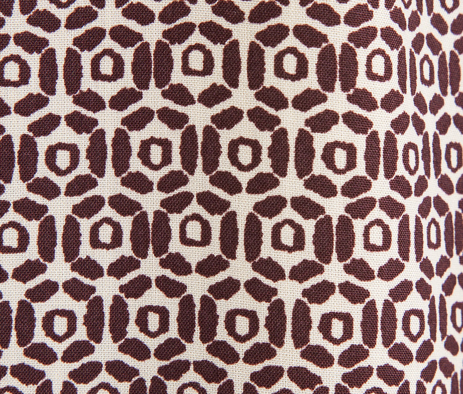 Detailní záběr na látku s hnědým geometrickým vzorem na béžovém pozadí.