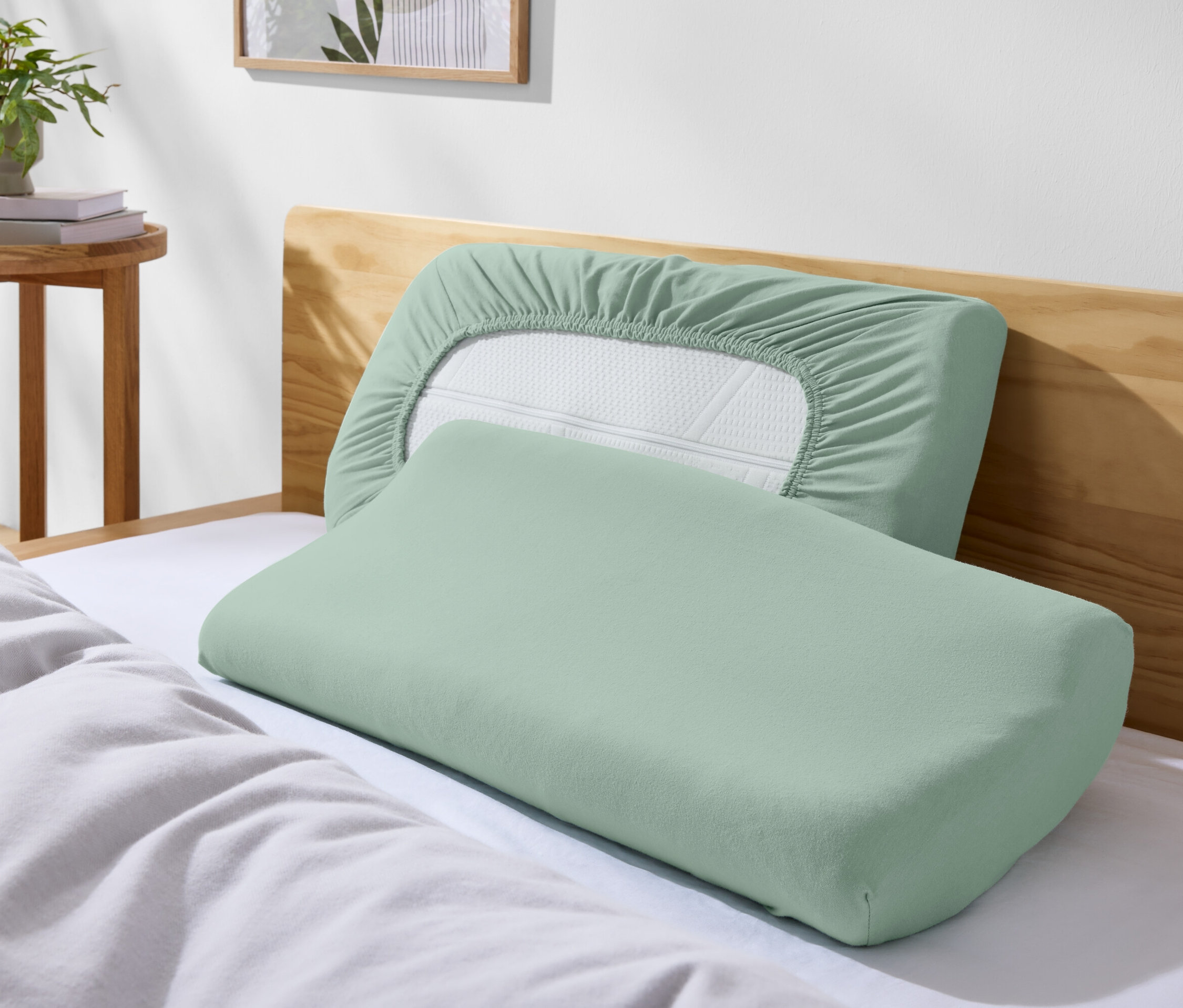 Dva zelené polštáře na posteli s bílým povlečením.