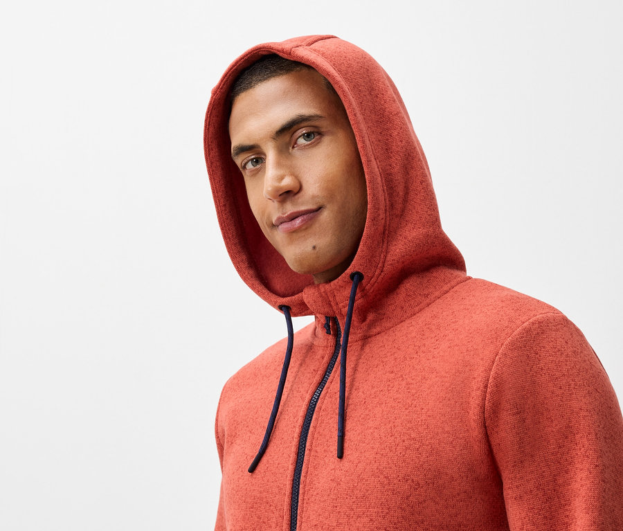 Portrét muže s kapucí s tmavě modrým zipem na oranžové mikině.