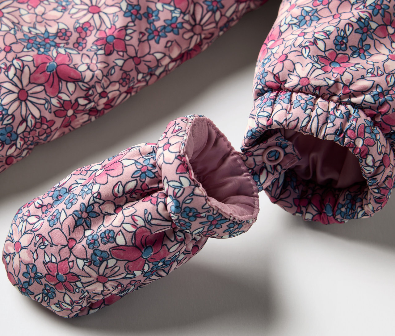 Detail zimního overalu pro miminka s květinovým vzorem a rukavicí.