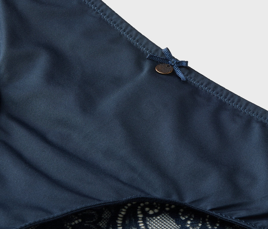 Detailní záběr na tmavě modré kalhotky s krajkou a mašlí.