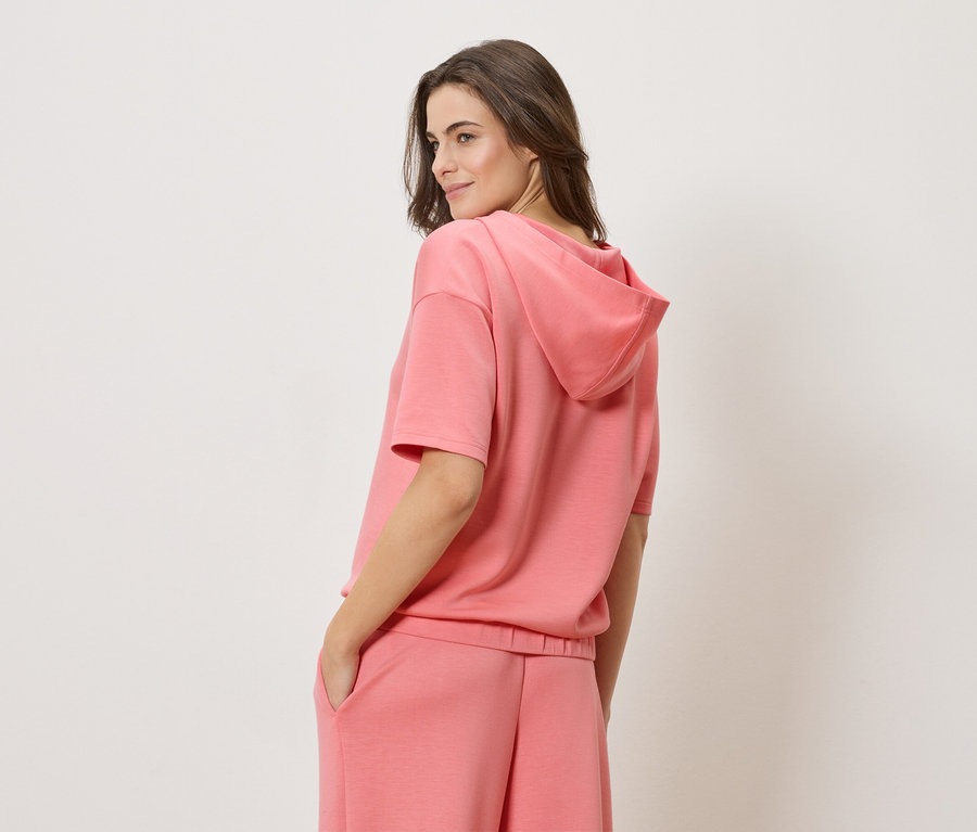 Žena má na sobě korálovou mikinu s krátkým rukávem a odpovídající korálové šortky.