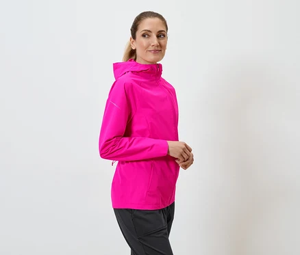 Žena s culíkem má na sobě růžovou bundu s kapucí a černé kalhoty na bílém pozadí.