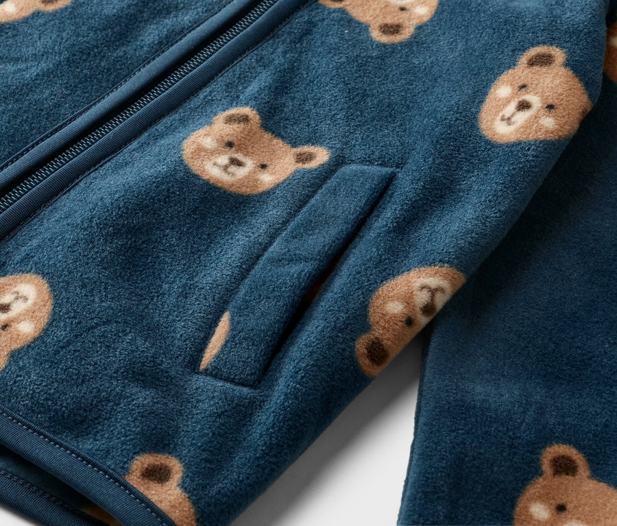 Detail modré fleecové bundy na zip s obličeji medvědů.