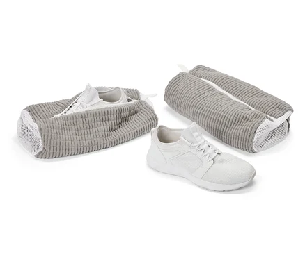 Bílá sportovní bota před šedou taškou na boty. Další bota je v otevřené tašce, třetí taška je zavřená.