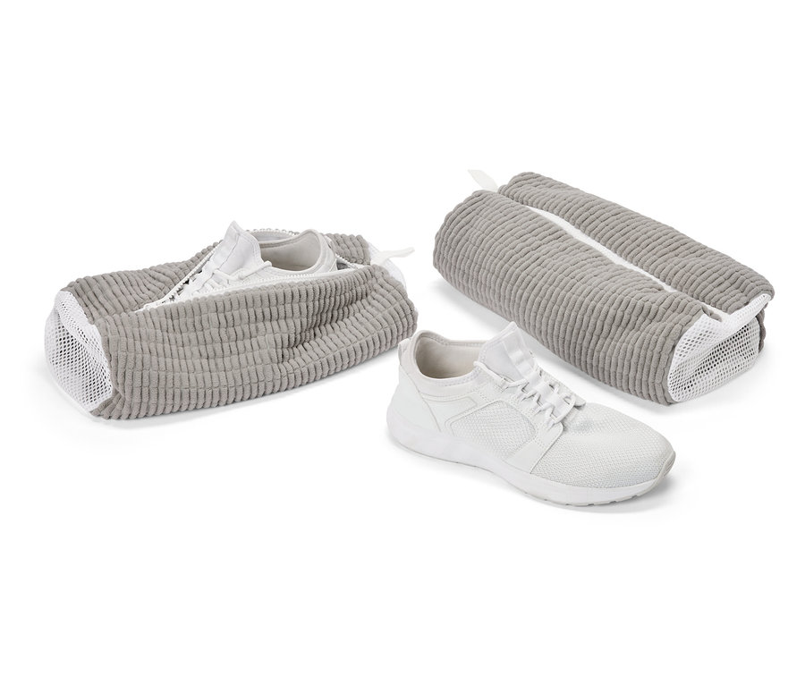 Bílá sportovní bota před šedou taškou na boty. Další bota je v otevřené tašce, třetí taška je zavřená.