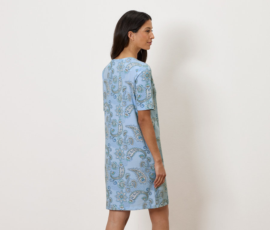 Žena stojí bokem a má na sobě světle modré květované šaty.
