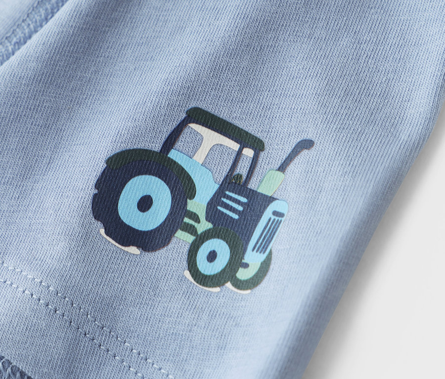 Detailní záběr světle modré látky s potiskem traktoru.