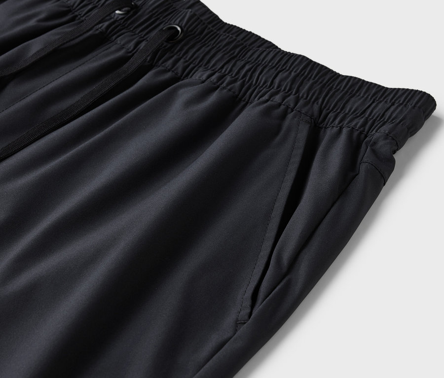 Detailní záběr na černé tepláky s elastickým pasem a stahovací šňůrkou.