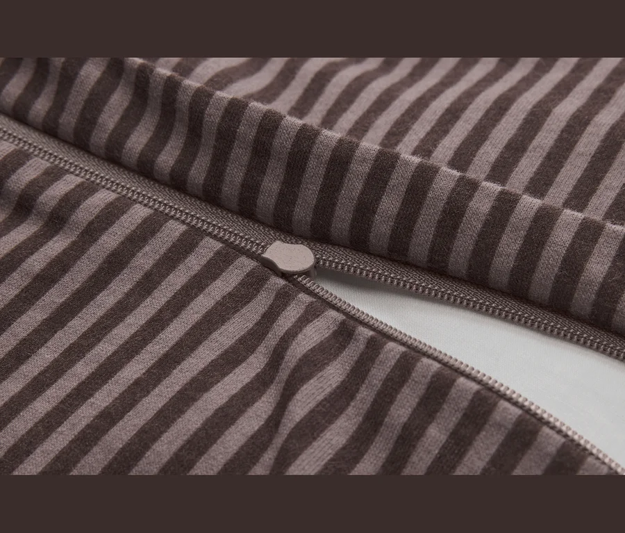 Detail hnědo-béžové pruhované látky s částečně otevřeným zipem a viditelným jezdcem.