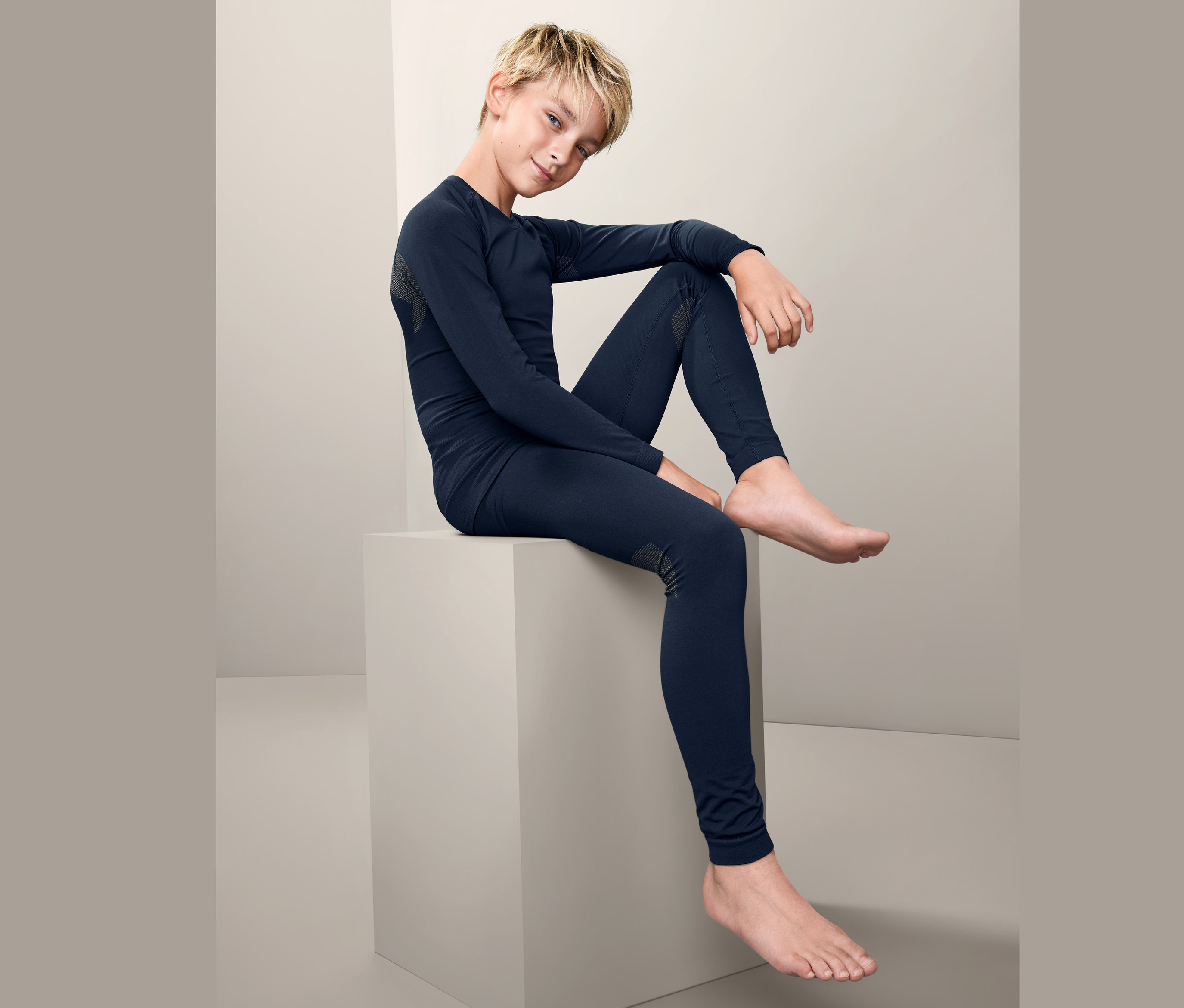 Chlapec sedí na kostce a má na sobě bezešvé funkční spodní prádlo.