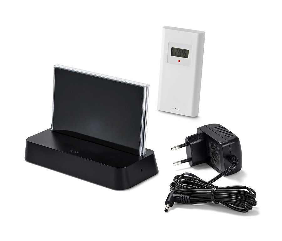 Černá meteostanice s barevným LCD displejem, řízená rádiovým signálem, bílý senzor a černý napájecí adaptér na bílém pozadí.