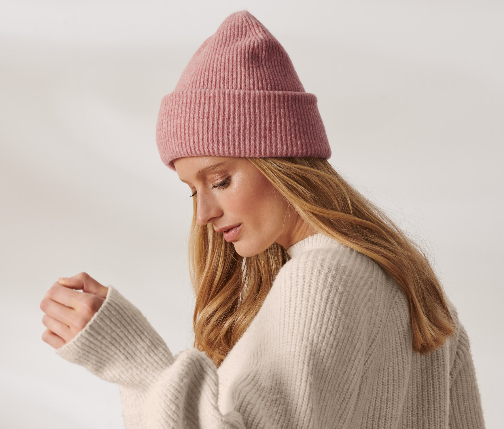 Blondýna s růžovou pletenou čepicí s vlnou a krémovým svetrem.
