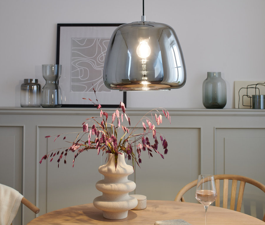 Chromové závěsné svítidlo nad stolem s vázou a sklenicí vína.