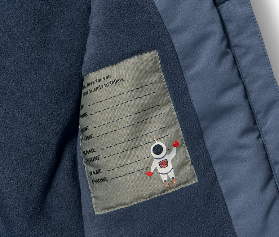 Detail dětské zimní kombinézy s vnitřní kapsou a štítkem pro jméno a telefon.