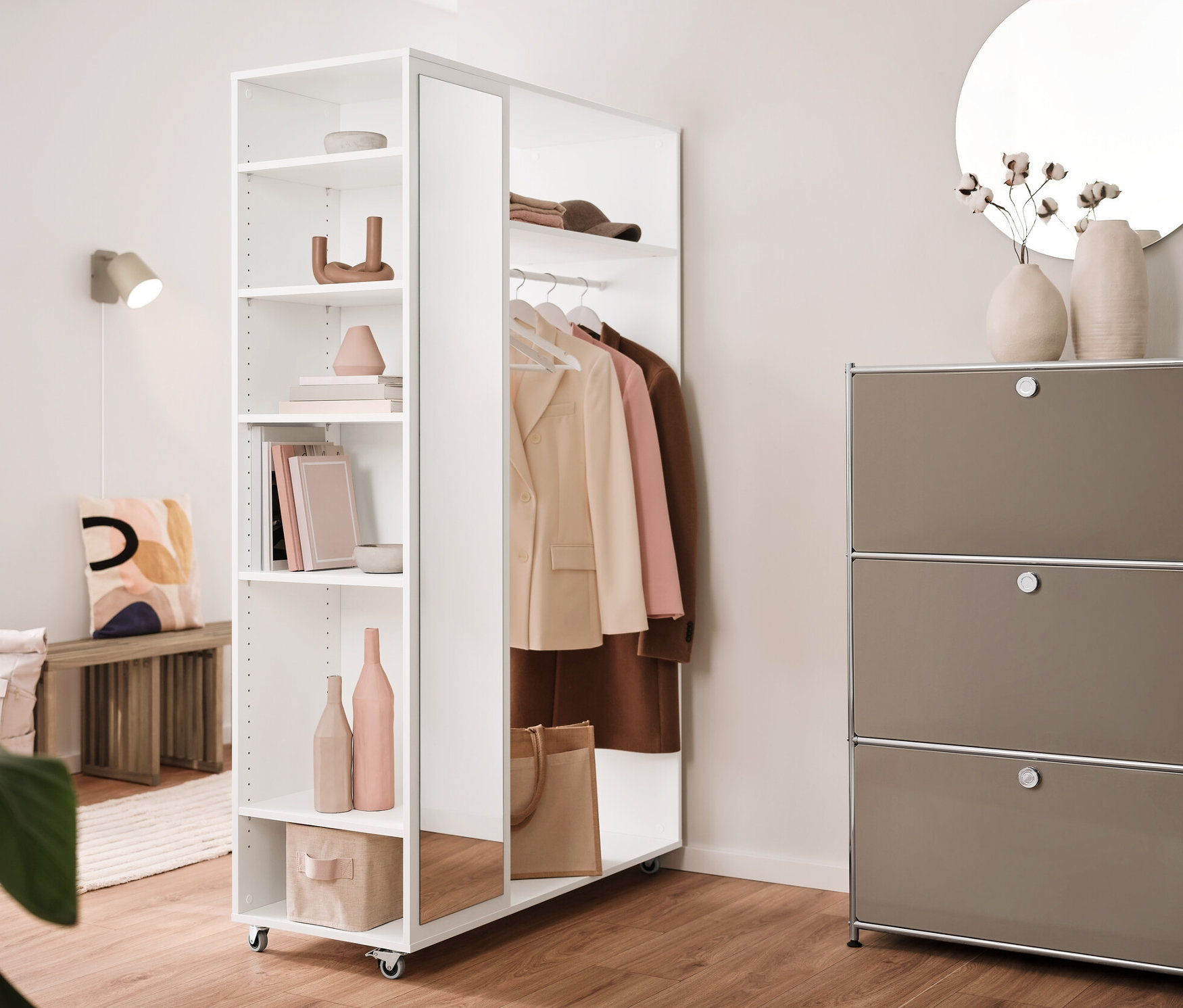 Interiér s rozkládací lavicí, mobilní šatní skříní se zrcadlem, kovovým regálem »CN3« se 3 výklopnými dvířky a krémovým kovovým nástěnným svítidlem.