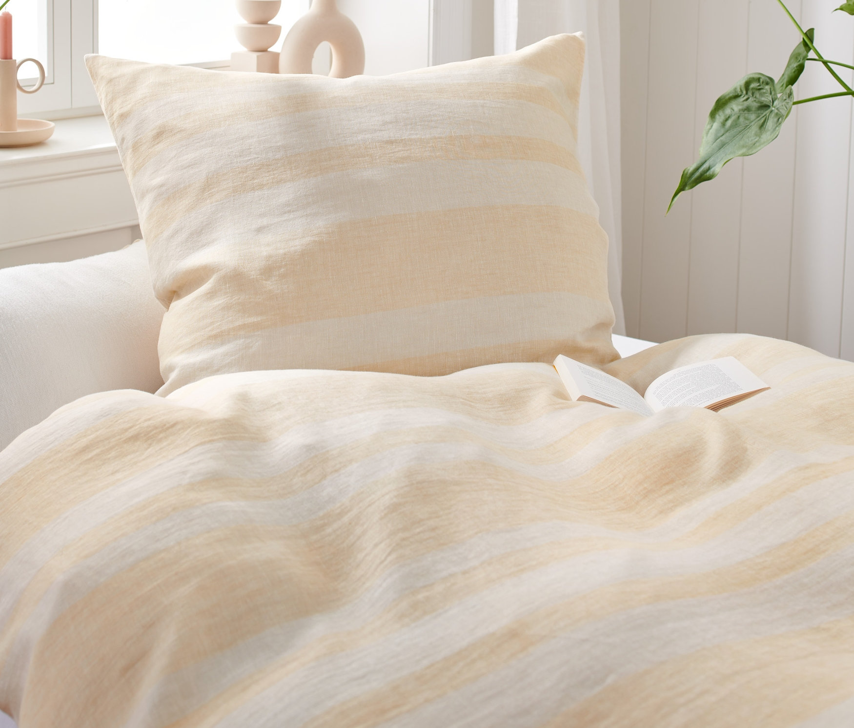 Pohled zblízka na postel s povlečením ze sepraného lnu s otevřenou knihou.