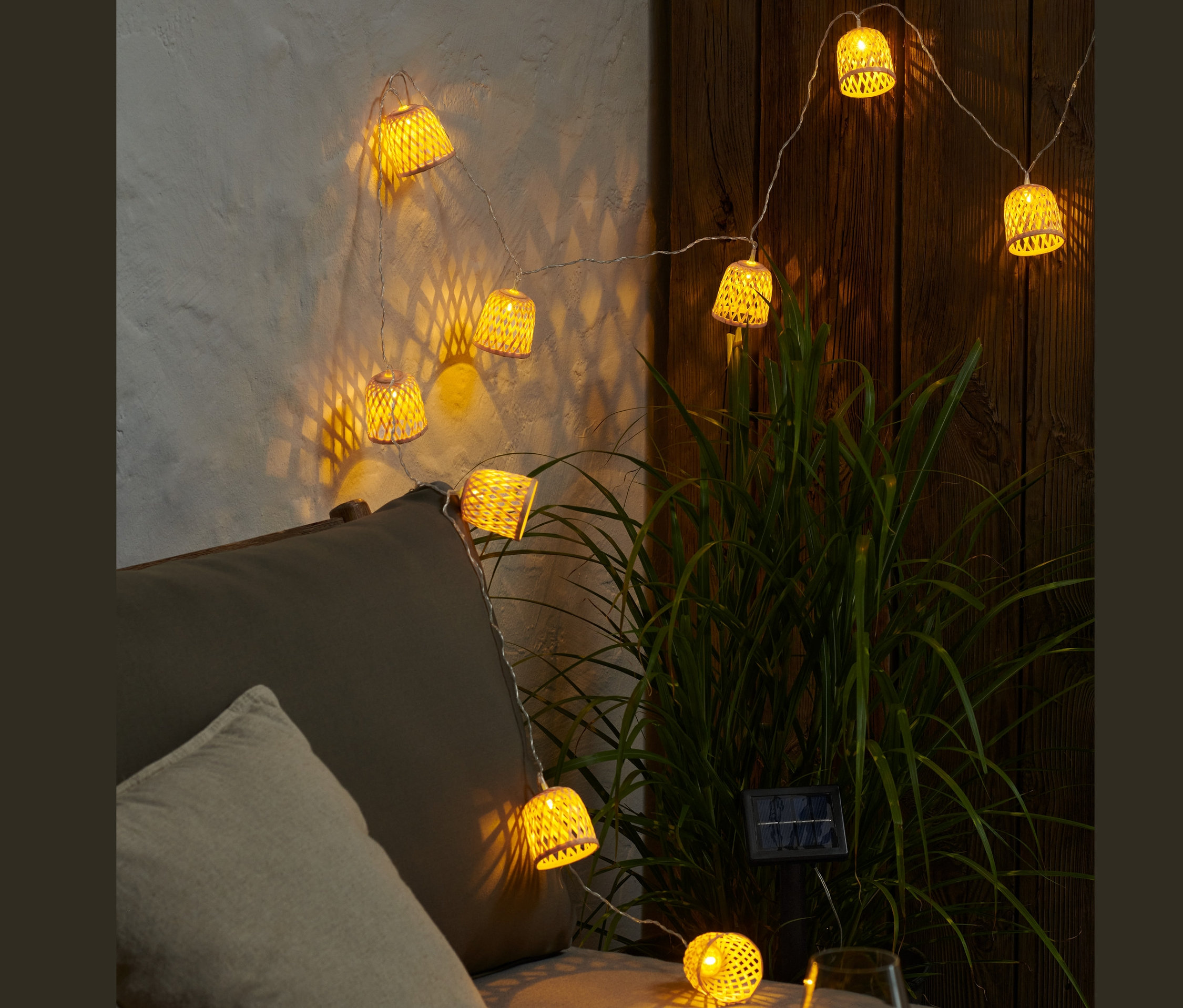Rozsvícený solární světelný řetěz s ozdobnými stínidly visí nad šedou pohovkou.