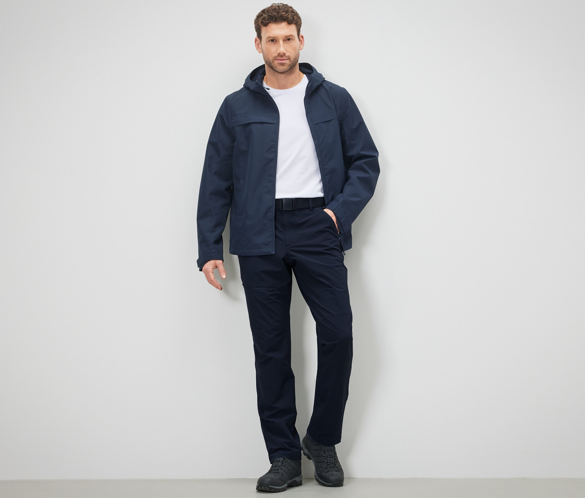 Muž stojí a pózuje na sobě outdoorové kalhoty a bundu.