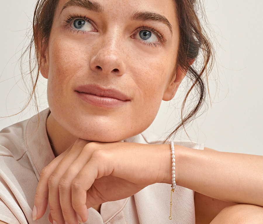 Žena se dívá nahoru a má na sobě náramek ze zlaceného stříbra 925/1000 se sladkovodními perlami z řízeného chovu.